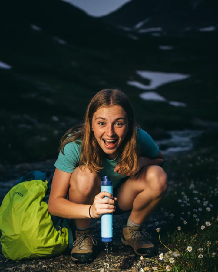 A person drinking through the KARST filter straw at a snowmelt rivulet crossing